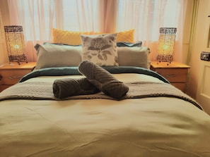 Una cama bien hecha con una colcha, almohadas y un par de calcetines doblados.