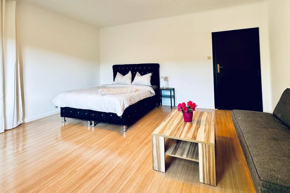 A modern bedroom with a bed, a wooden coffee table, and a grey sofa.