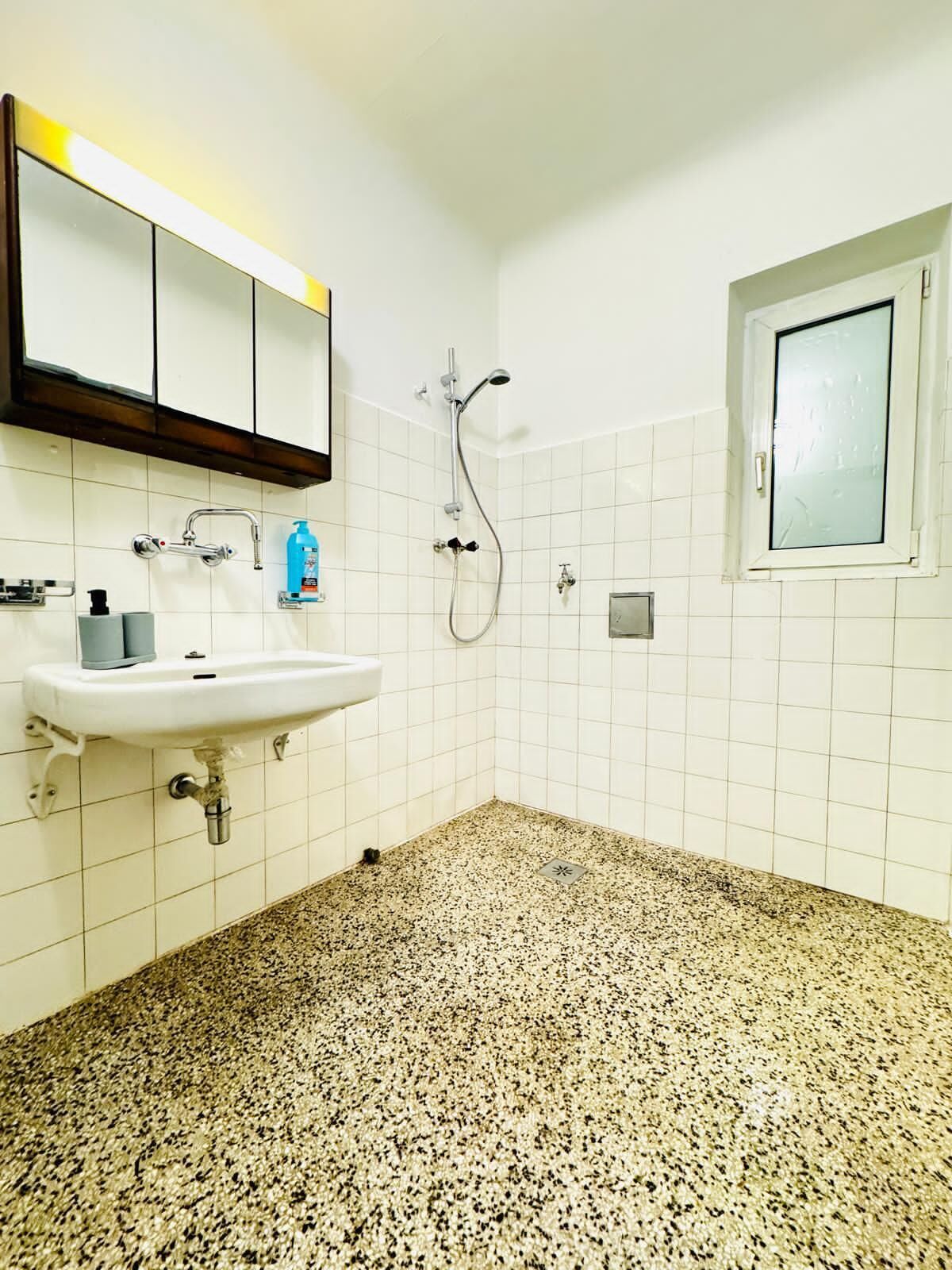 Une salle de bain avec un lavabo blanc, une douche et une fenêtre.