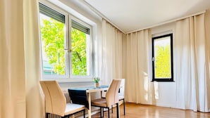 Tilava huone, jossa on puulattia, ruokapöytä tuoleineen ja suuret ikkunat, joissa on verhot.