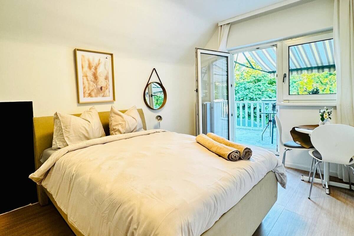 A bedroom with a bed, a desk, and a chair near a window with a view of greenery.