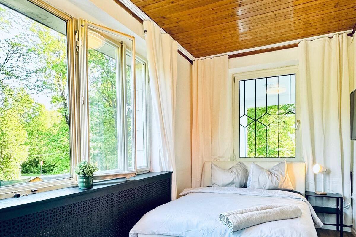 A bedroom with a large bed, a window with curtains, a radiator, and a ceiling light.