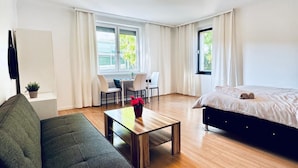 Moderni hotellihuone, jossa on sänky, sohva, ruokapöytä tuoleineen ja pieni keittiöalue.
