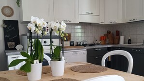 A modern kitchen with white cabinets, a wooden dining table, and white chairs. There are potted plants on the table and a hanging light fixture above. - Villa le palme, 500 mt from the beaches of Sas Linnas Siccas Bay. (Orosei)