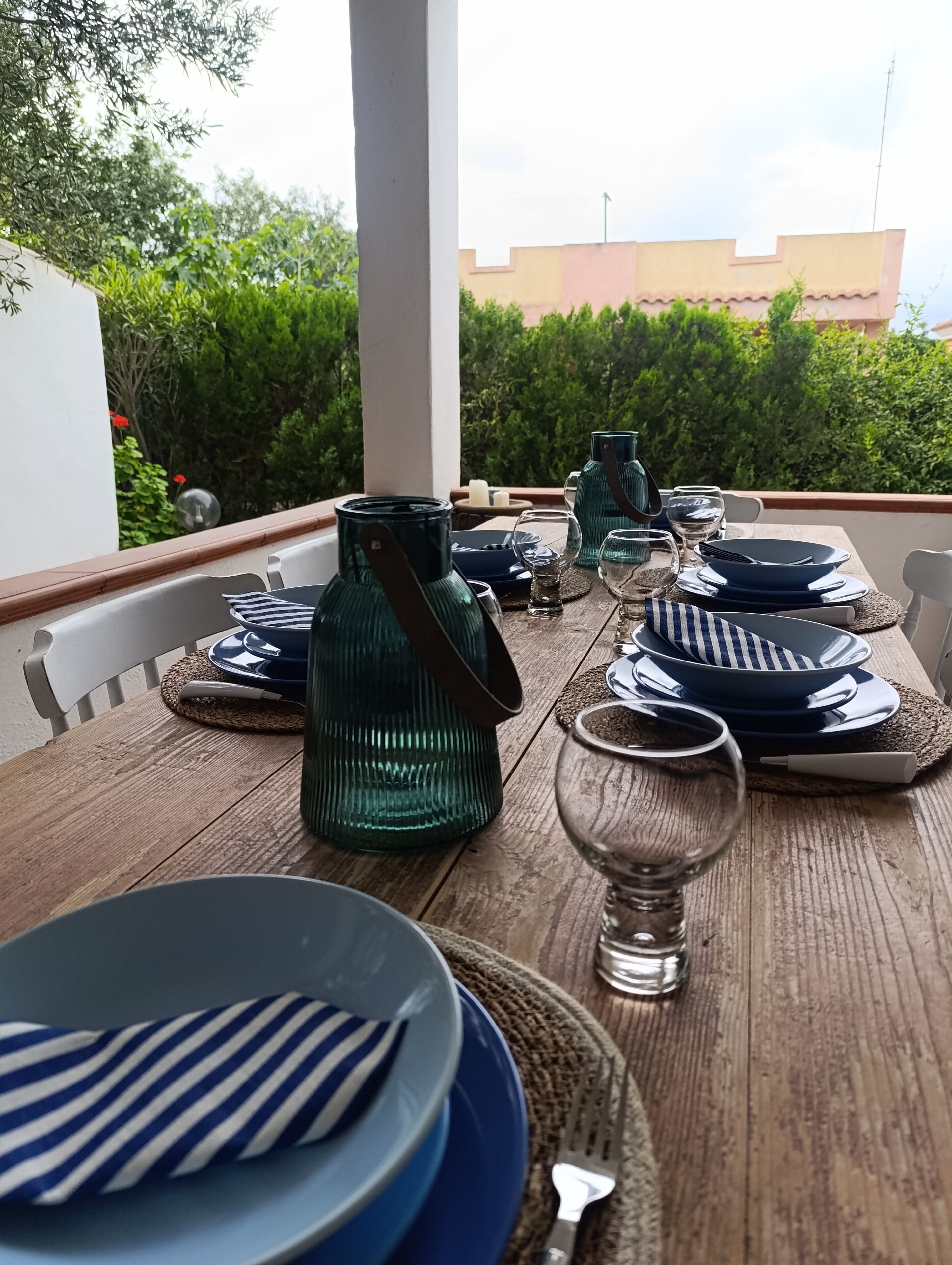 A dining table set outdoors with plates, glasses, and a green vase.