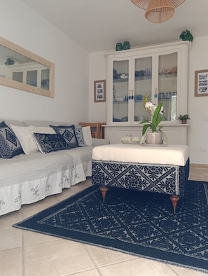 Une pièce avec un canapé blanc, un pouf à motifs, un meuble avec des portes en verre et un tapis bleu.