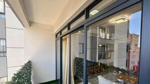 Un edificio moderno con amplios ventanales, un balcón con planta en maceta y vistas a la ciudad.