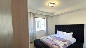 Ein Hotelzimmer mit einem großen Bett, einem Fenster mit Vorhängen und einer Deckenleuchte.