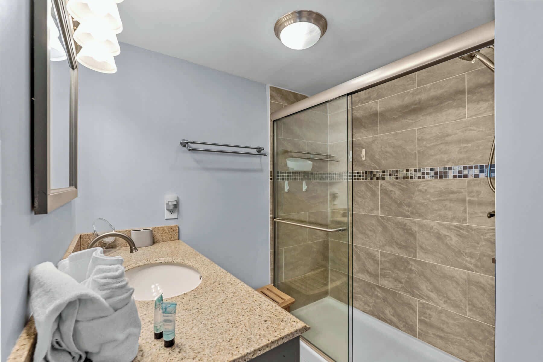 A bathroom with a granite countertop, a white sink, a glass shower enclosure, and a towel rack.