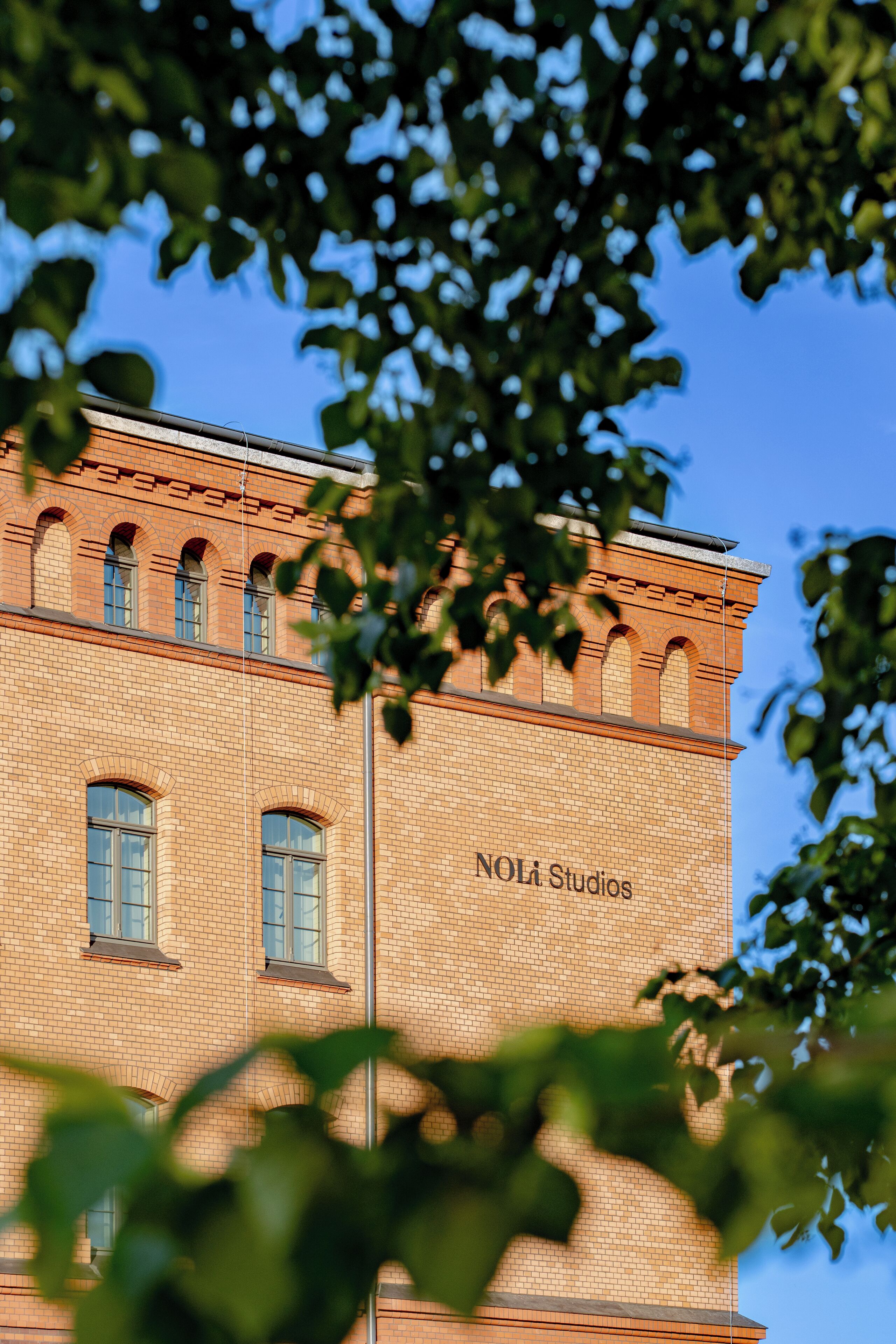 En byggnad i tegel med välvda fönster och texten ”NOLi Studios” på fasaden.