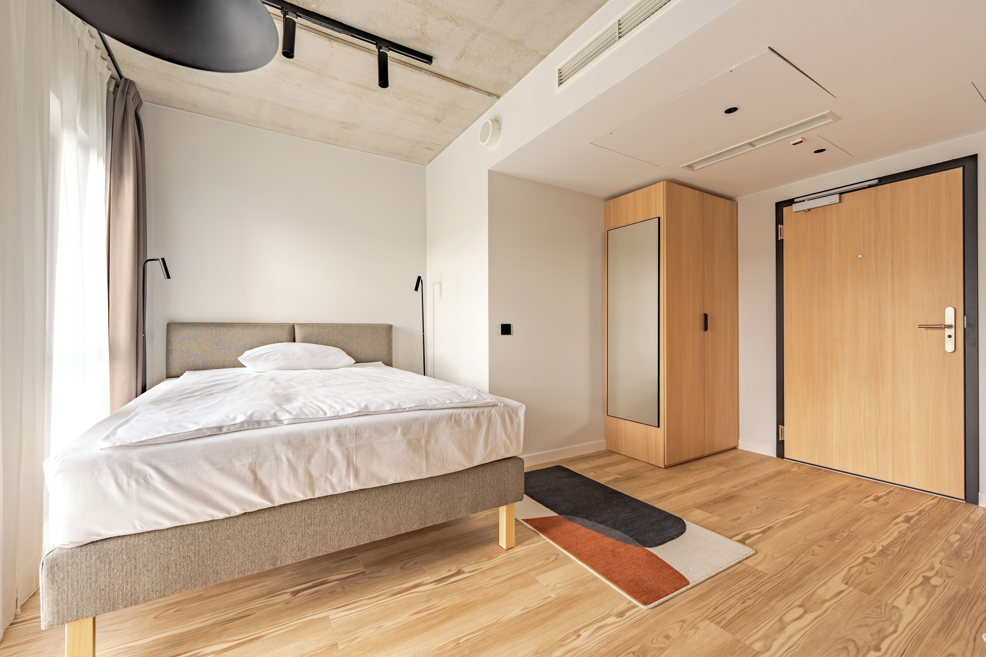 A modern bedroom with a bed, a wardrobe, and a door.
