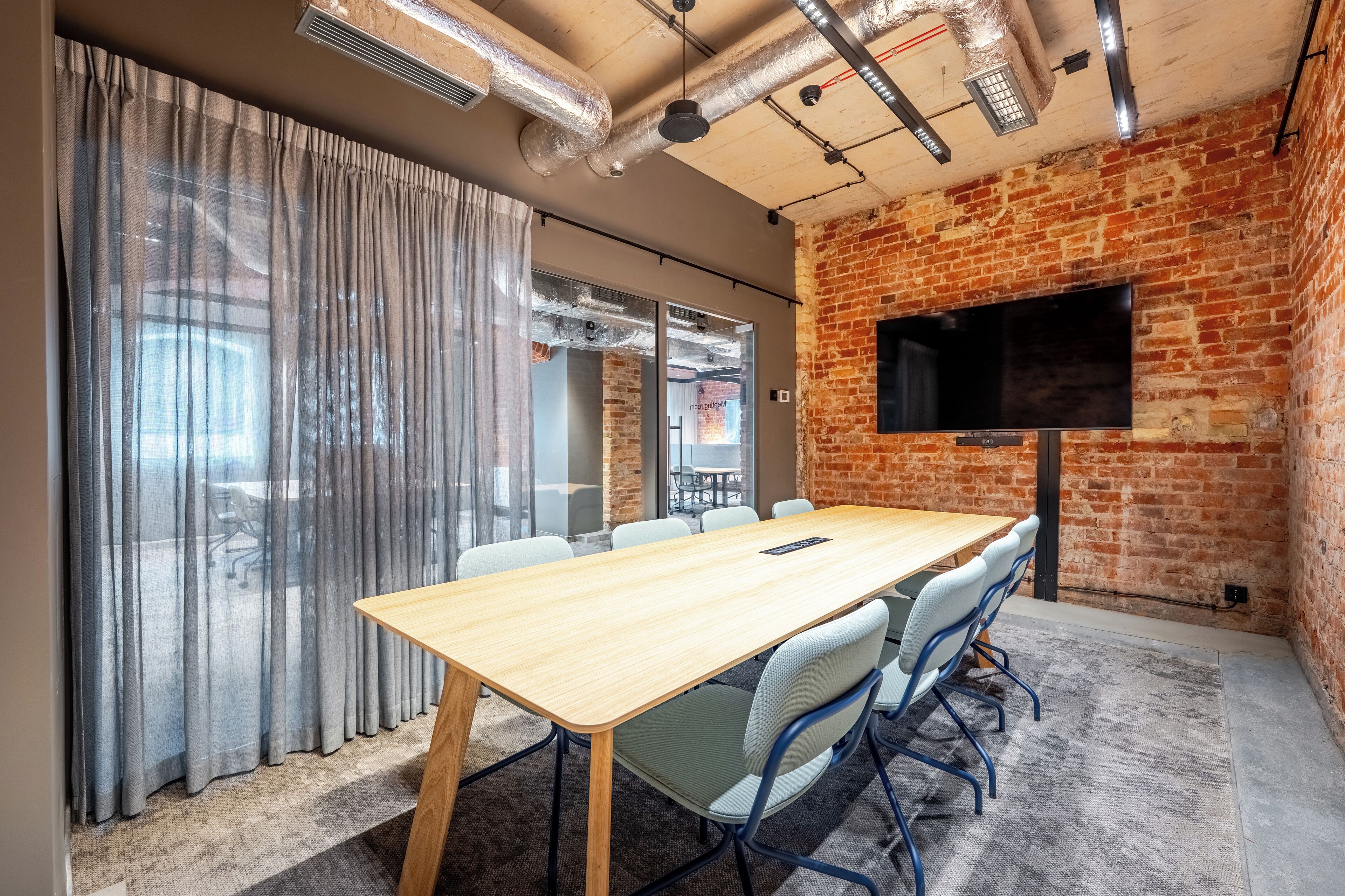 Une salle de conférence avec une longue table, des chaises, un téléviseur et un mur en briques.