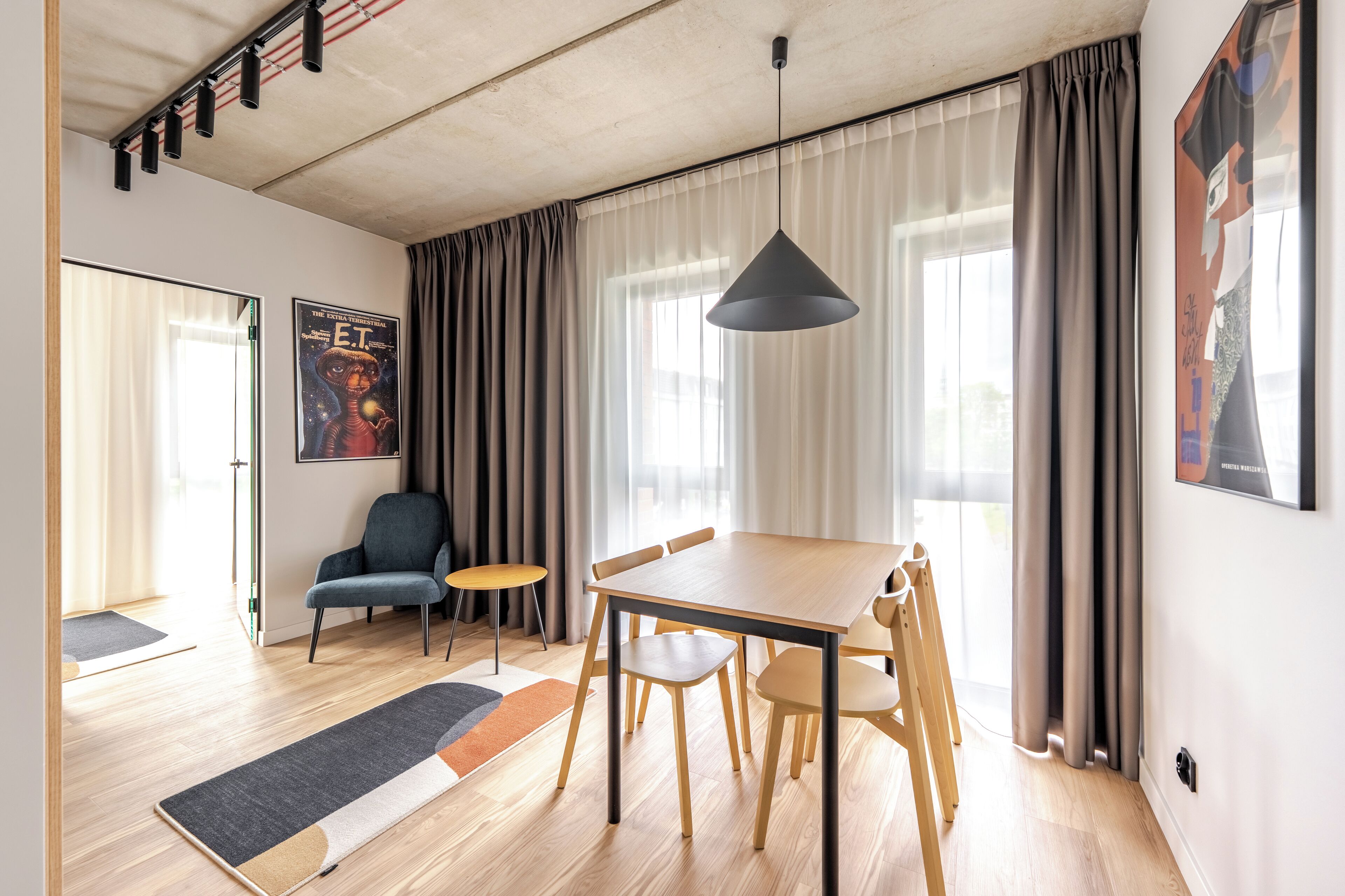 A modern living room with a wooden dining table, chairs, a sofa, and a large window with curtains.