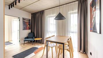 A modern living room with a wooden dining table, chairs, a sofa, and a large window with curtains.