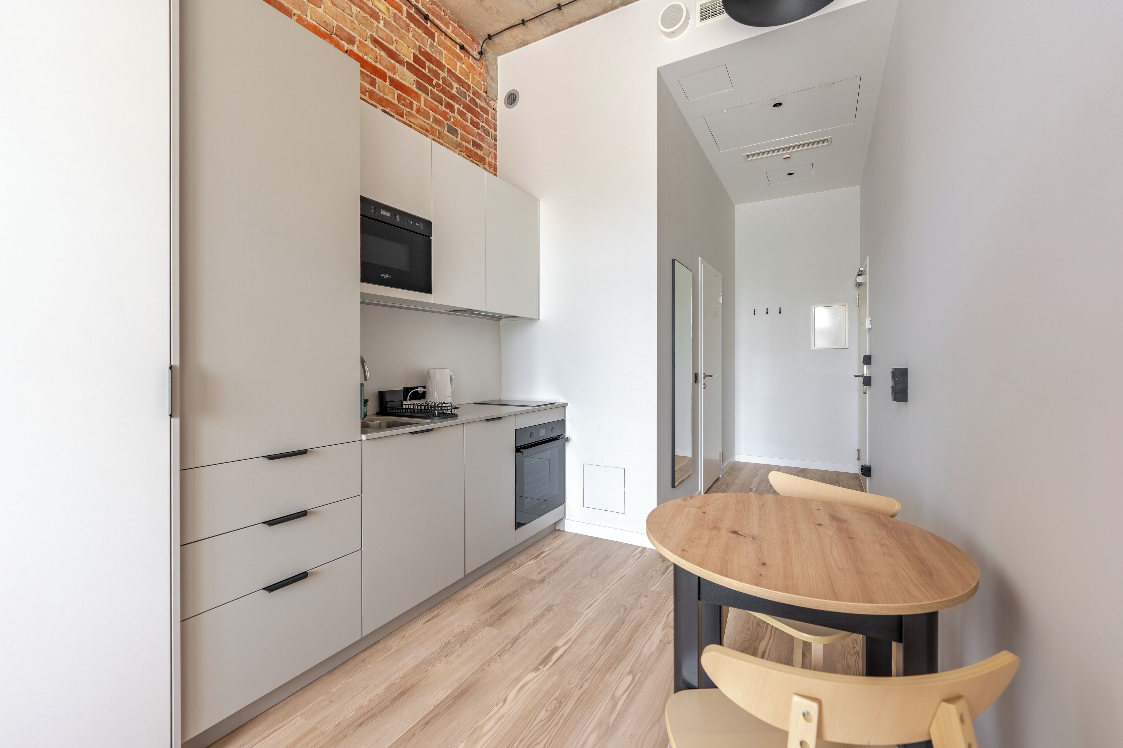 A modern kitchen with white cabinets, a brick accent wall, and a wooden dining table with chairs.