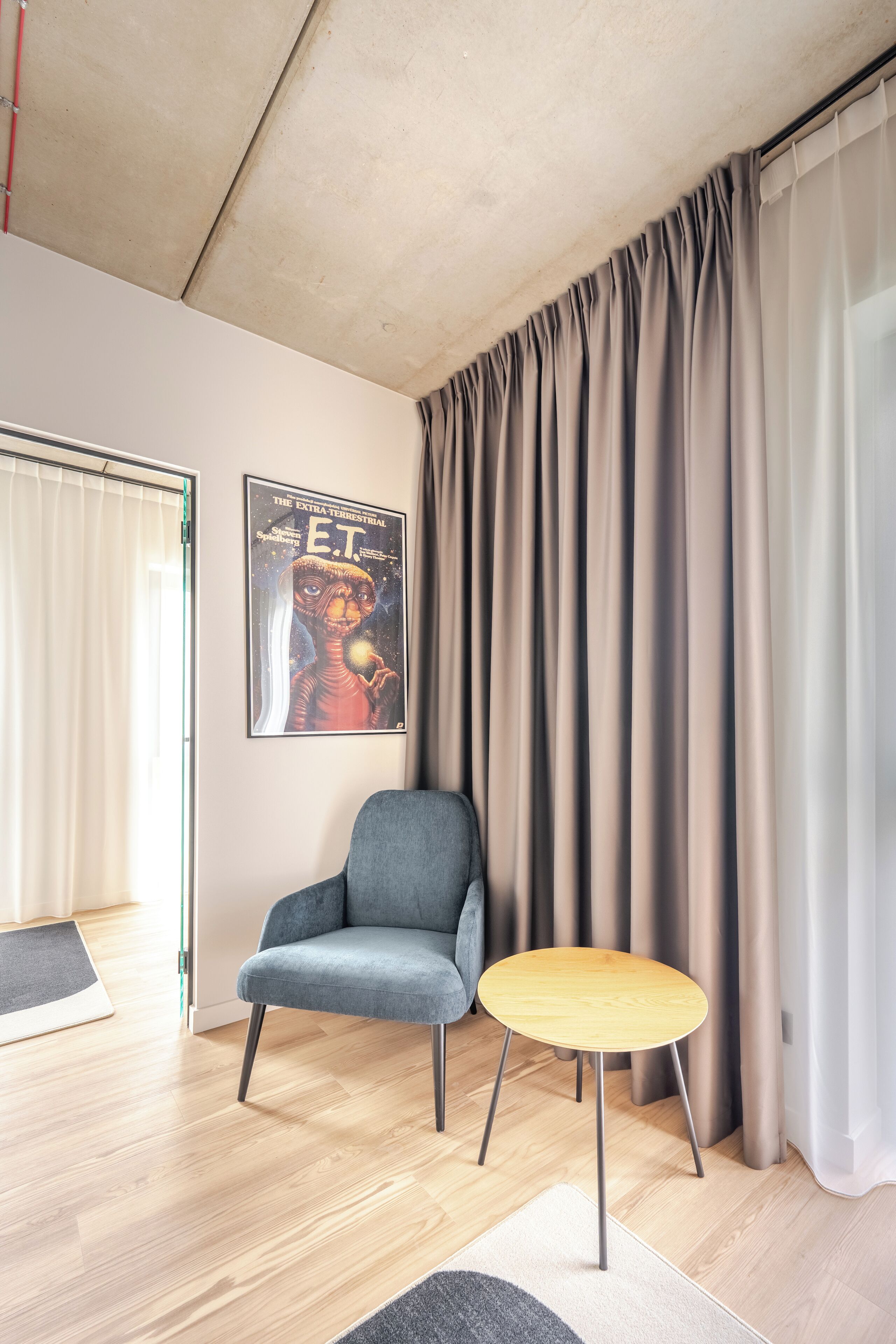 Una sala de estar moderna con un sillón gris, una pequeña mesa de madera y un cartel de una película de ciencia ficción en la pared.