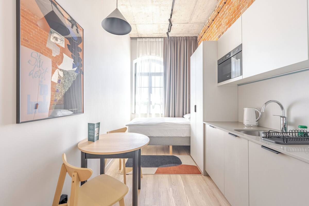 Une cuisine compacte avec un coin repas, un lit et une grande fenêtre avec des rideaux.
