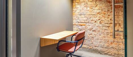 A room with a wooden desk, a red office chair, a brick wall, and a modern light fixture.