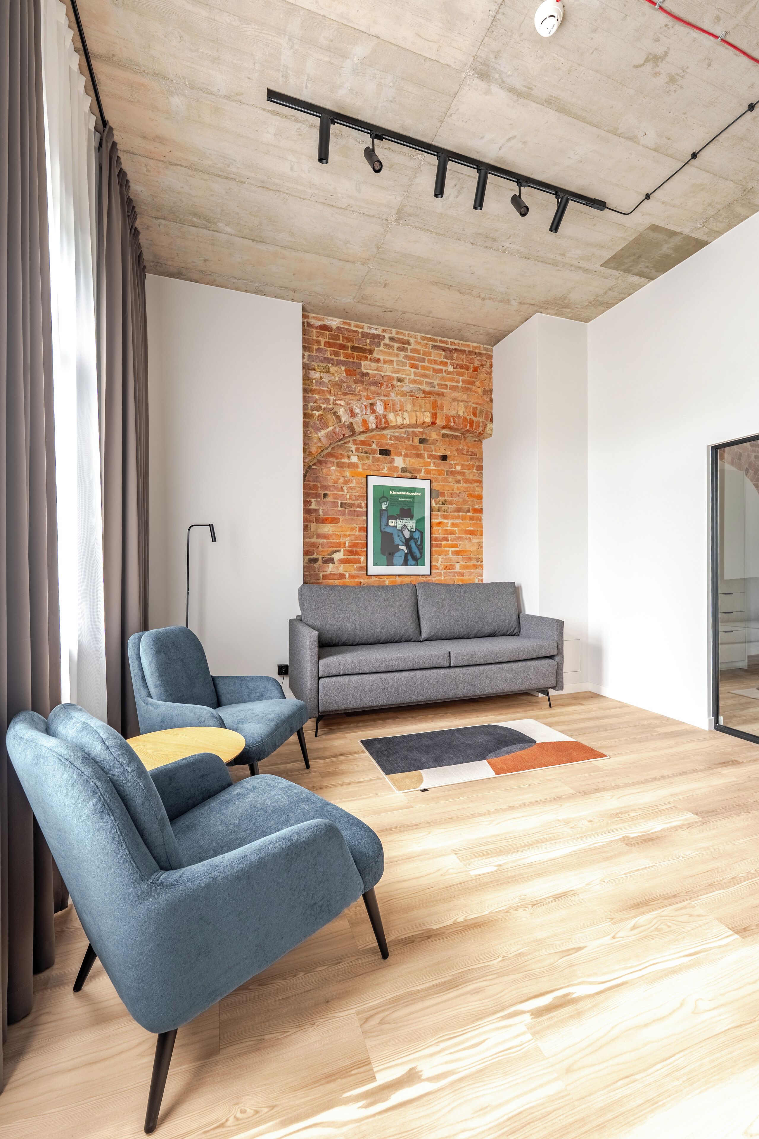 A modern living room with a brick wall, two grey sofas, and a wooden floor.