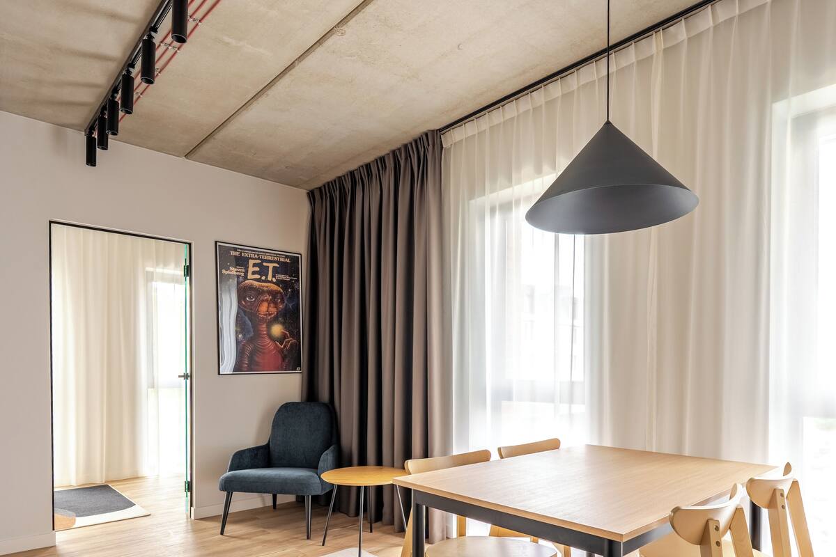 Un espace repas moderne avec une table et des chaises en bois, un luminaire suspendu et une affiche au mur.