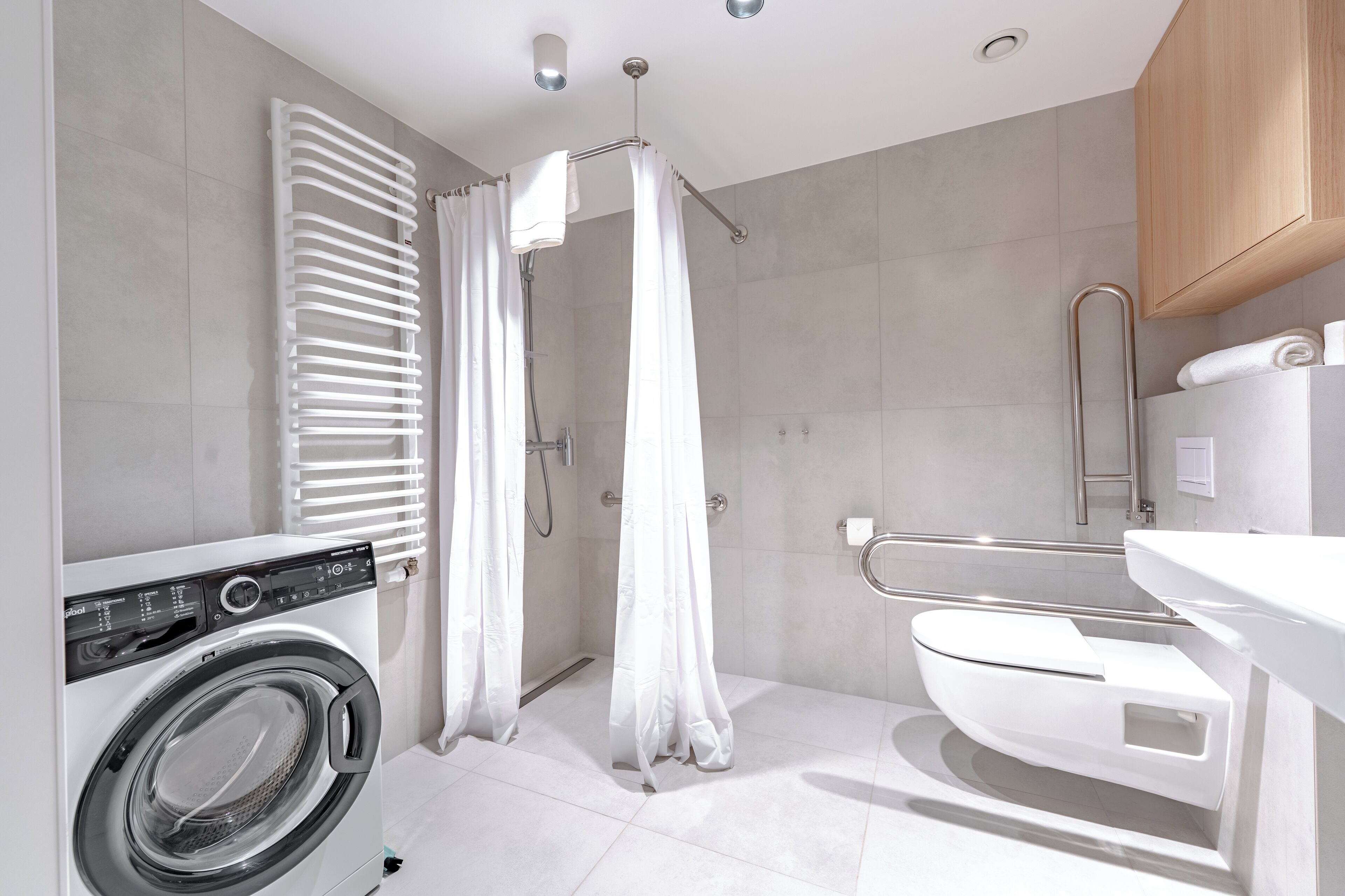 A modern bathroom with a built-in washing machine, a shower with a curtain, a toilet, and a wooden cabinet.