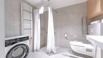 A modern bathroom with a built-in washing machine, a shower with a curtain, a toilet, and a wooden cabinet.