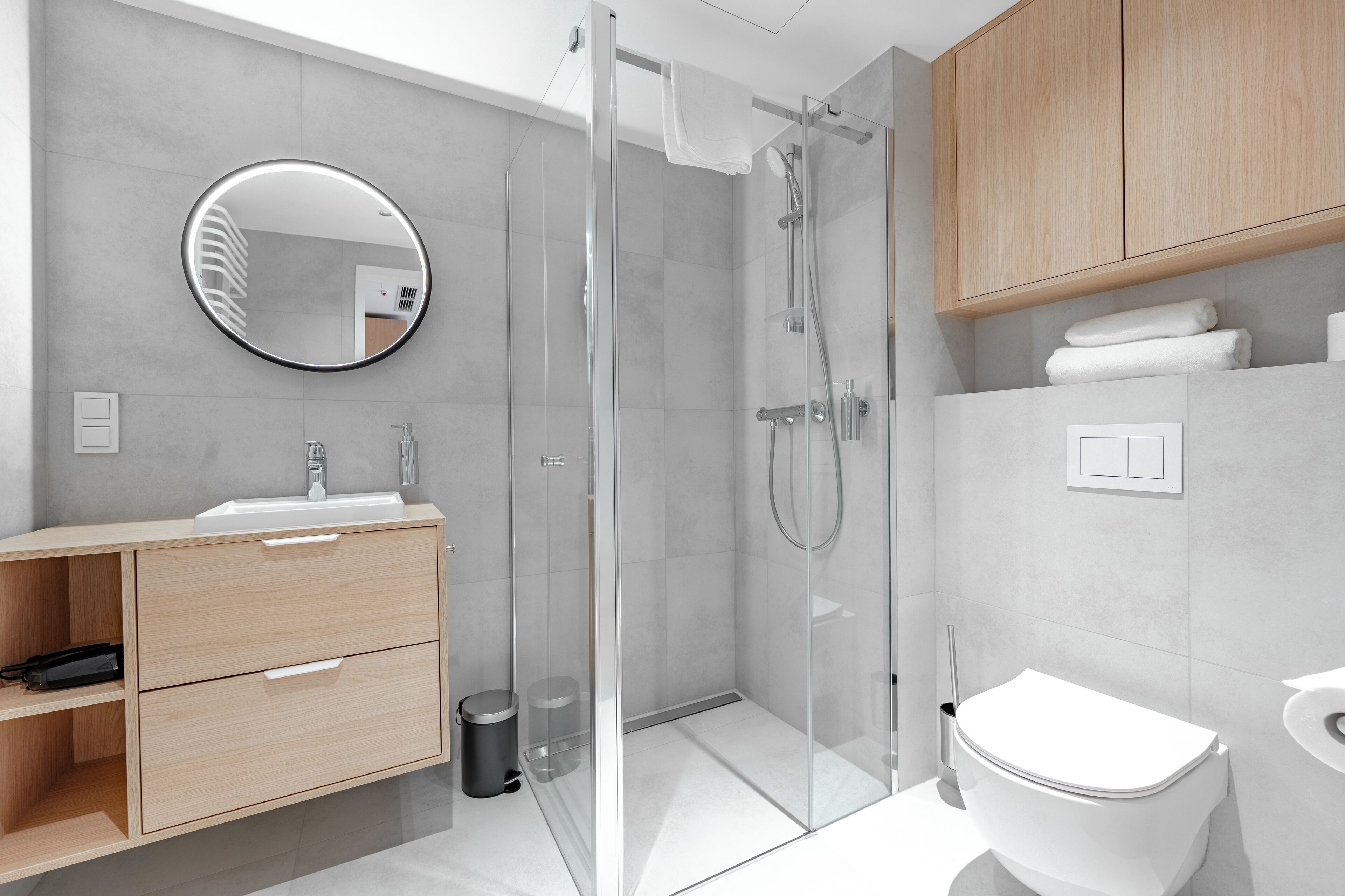 A modern bathroom with a glass-enclosed shower, a sink with a mirror, and wooden cabinets.