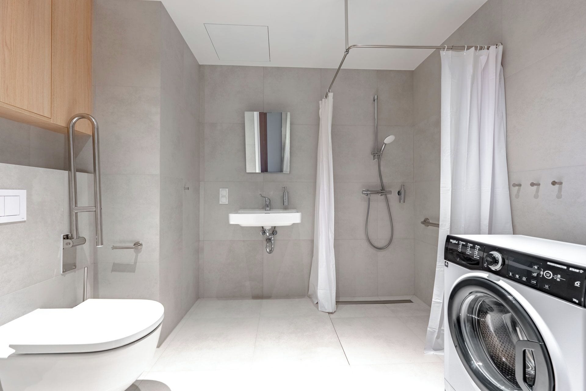 Ein modernes Badezimmer mit Toilette, Waschbecken, Dusche und einer Frontlader-Waschmaschine.