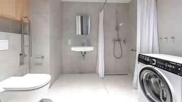 A modern bathroom with a toilet, sink, shower, and a front-loading washing machine.