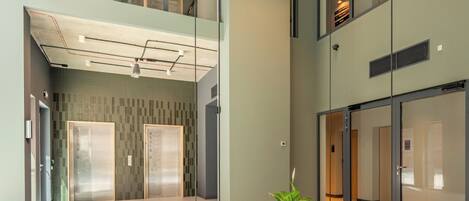 A spacious lobby with a modern design, featuring a central seating area, glass walls, and a high ceiling with exposed ductwork.