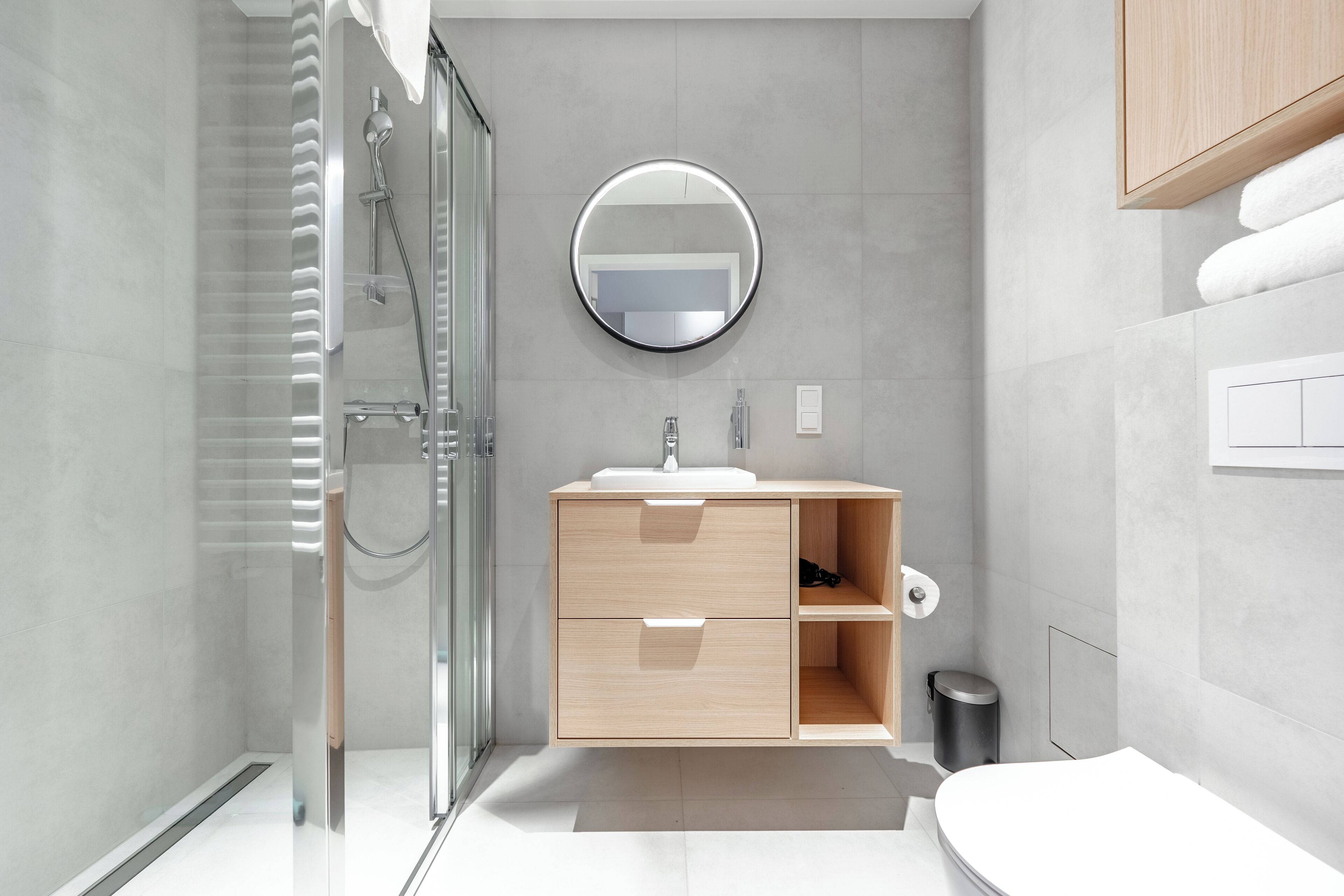 A modern bathroom with a glass shower enclosure, a wooden vanity with a sink, a mirror, and a toilet.