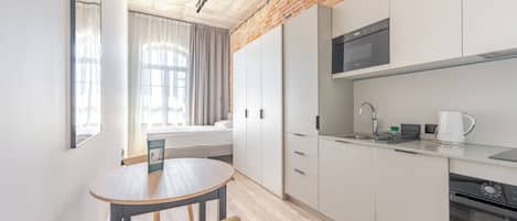Una cocina moderna con armarios blancos, horno empotrado y microondas. Hay una zona de comedor con una mesa redonda y sillas.