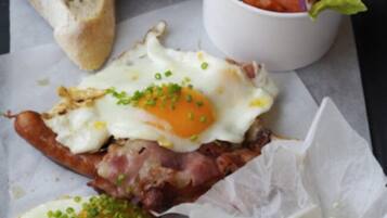 A sandwich with a fried egg, bacon, and green onions on a piece of bread, accompanied by a small salad and a cup of tomato soup.
