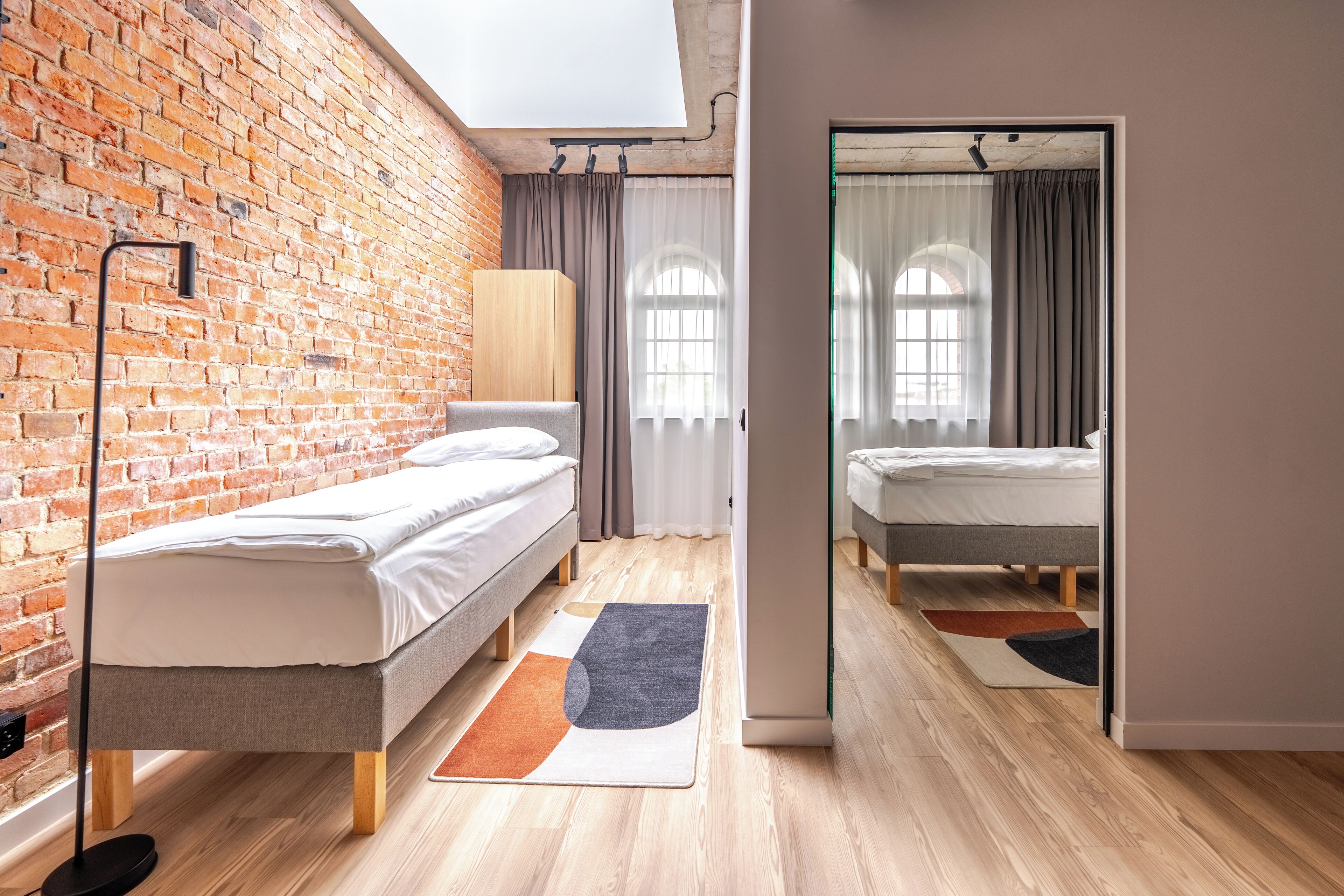 A modern room with a brick wall, two beds, a large mirror, and a wooden floor.