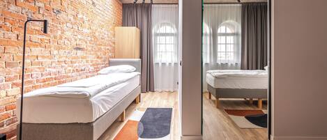A modern room with a brick wall, two beds, a large mirror, and a wooden floor.