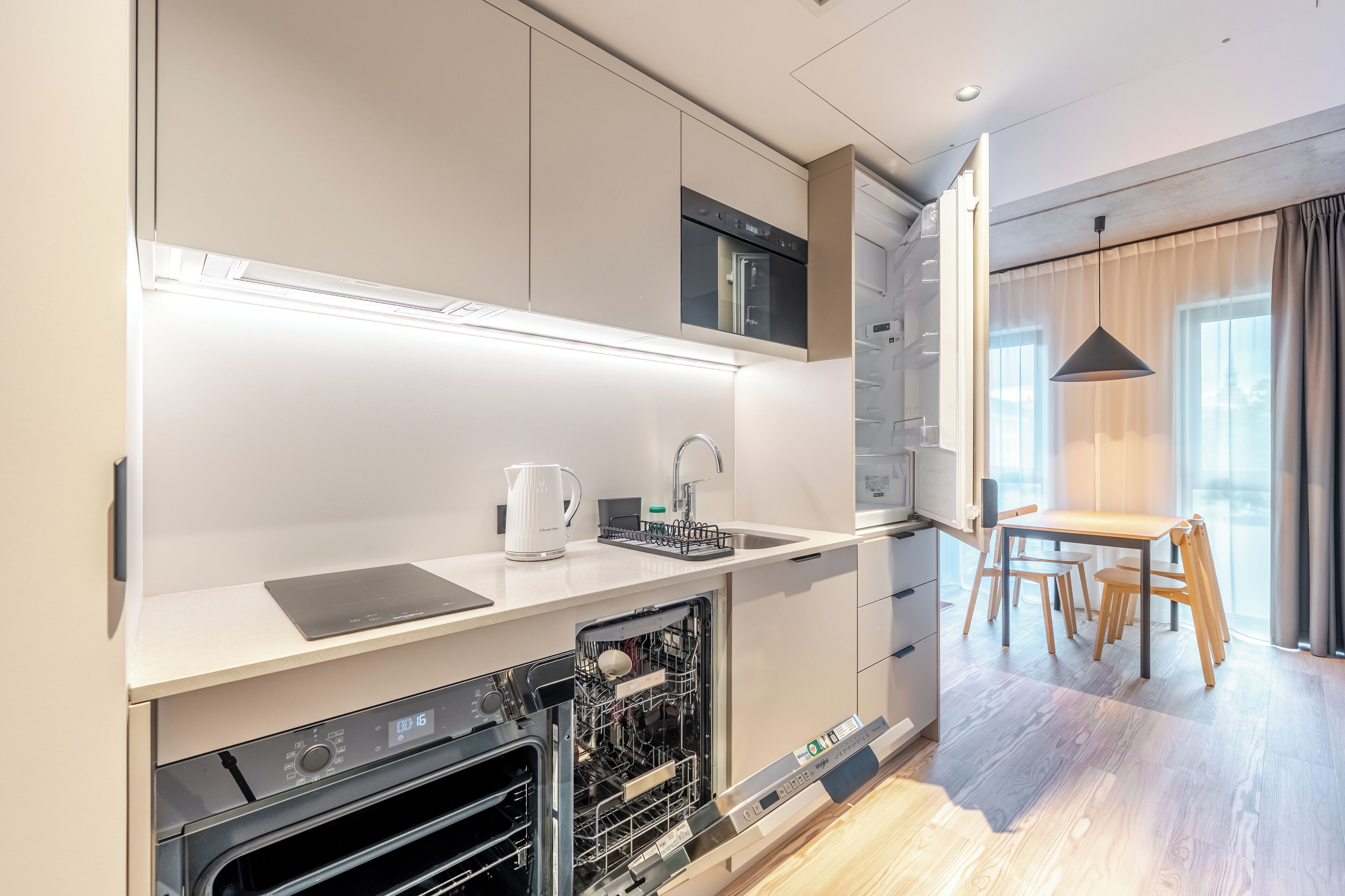Een moderne keuken met inbouwapparatuur, een vaatwasser en een eethoek met een tafel en stoelen.