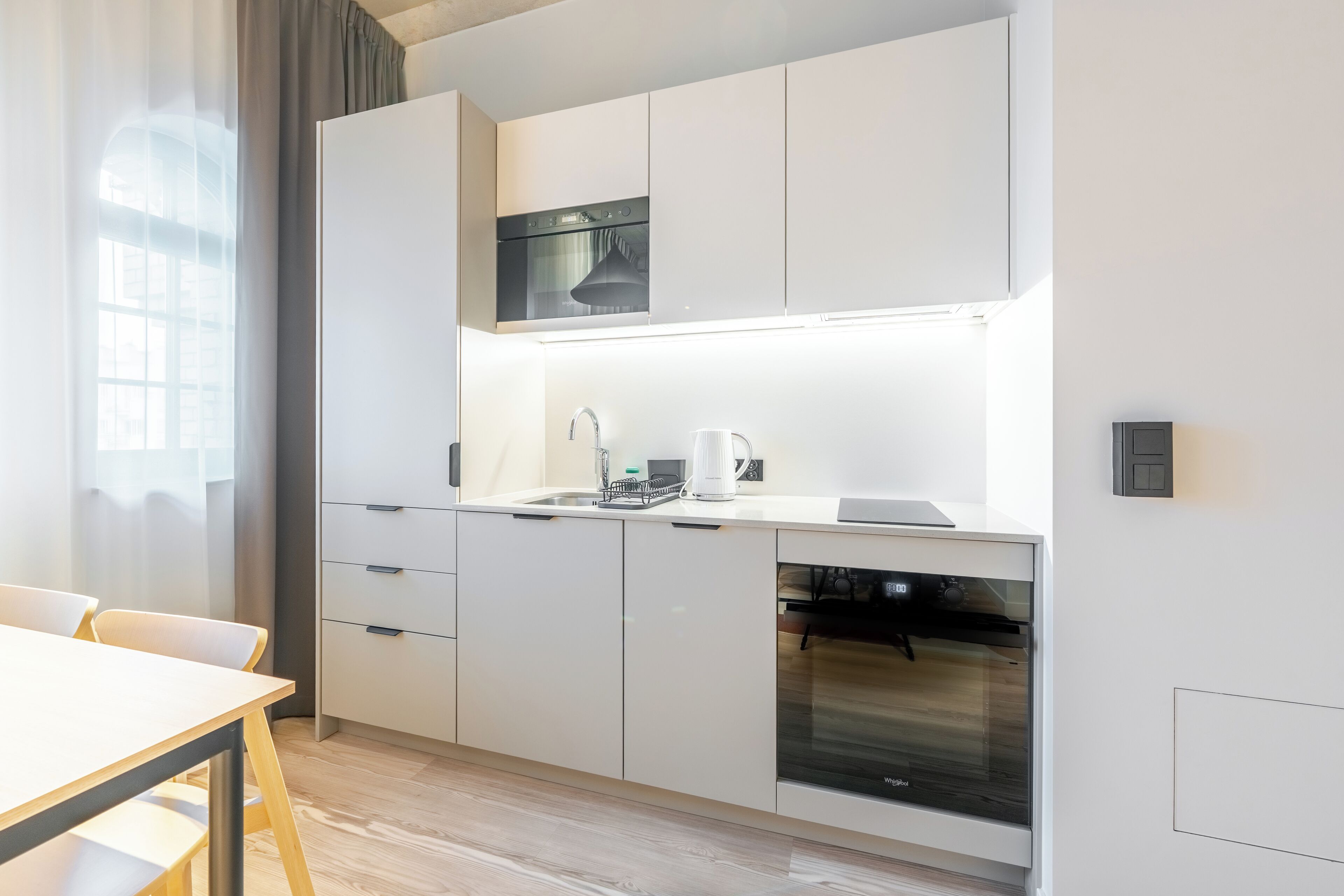 Una cocina moderna con armarios blancos, horno empotrado y lavavajillas.