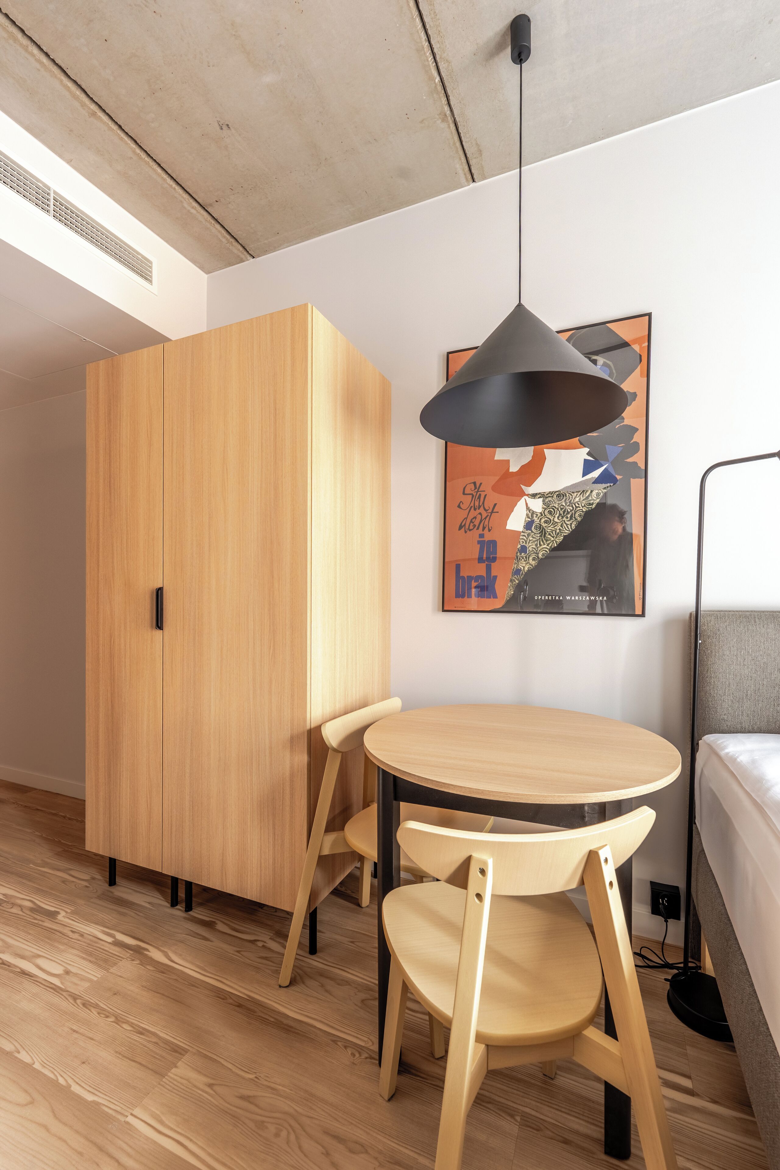 Una habitación moderna con un armario de madera, una mesa redonda de madera con dos sillas, una lámpara colgante y una obra de arte enmarcada en la pared.