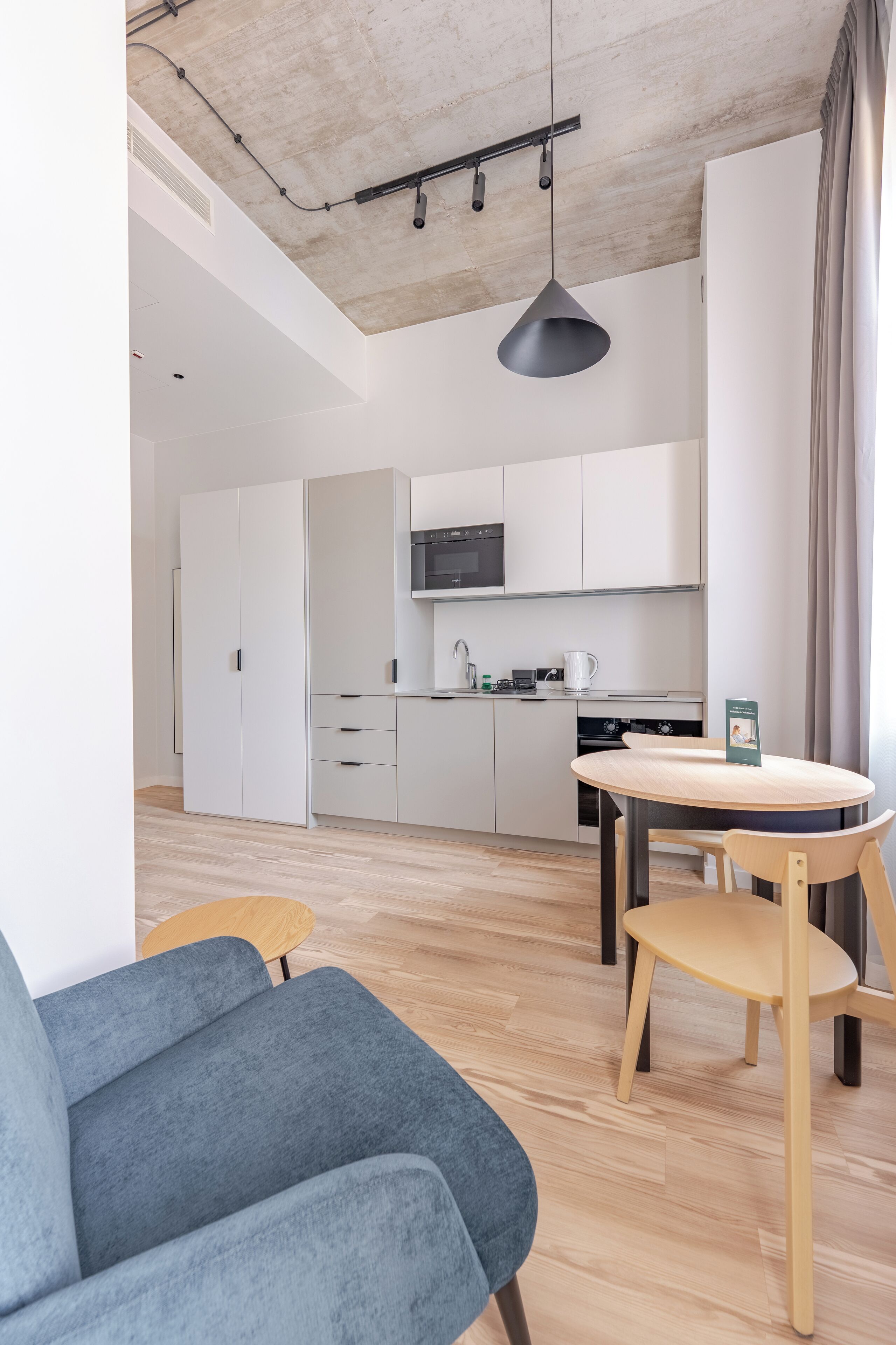 A modern kitchen with white cabinets, a microwave, and a coffee maker. There is a dining table with chairs and a blue sofa in the foreground.