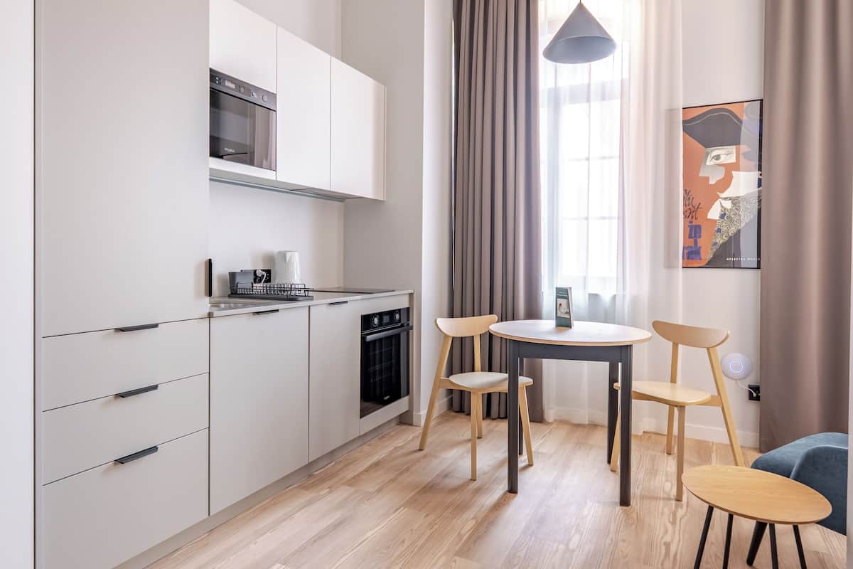 Une cuisine moderne avec des armoires blanches, un four encastré et un coin repas comprenant une table et des chaises.