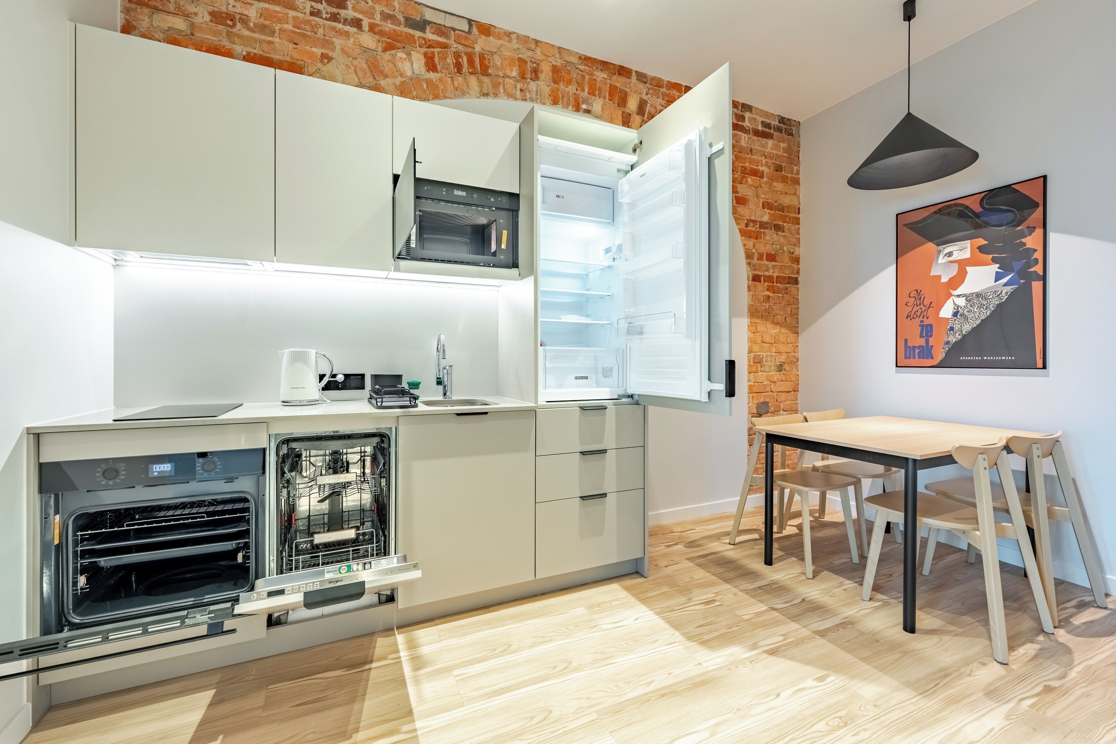 A modern kitchen with white cabinets, a built-in oven, and a dining area with a wooden table and chairs.