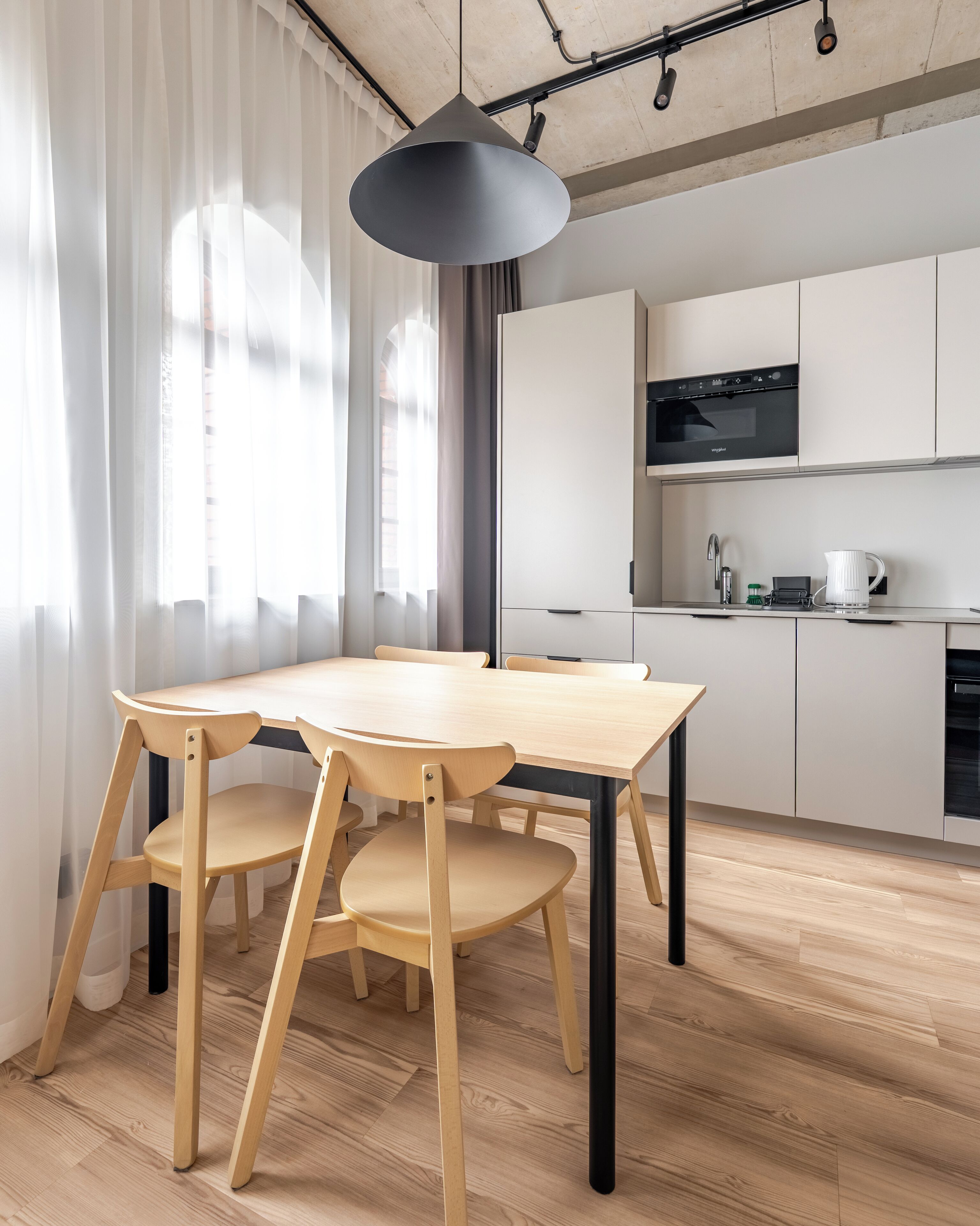 Una cocina moderna con armarios blancos, un microondas negro y una mesa de comedor de madera con sillas.