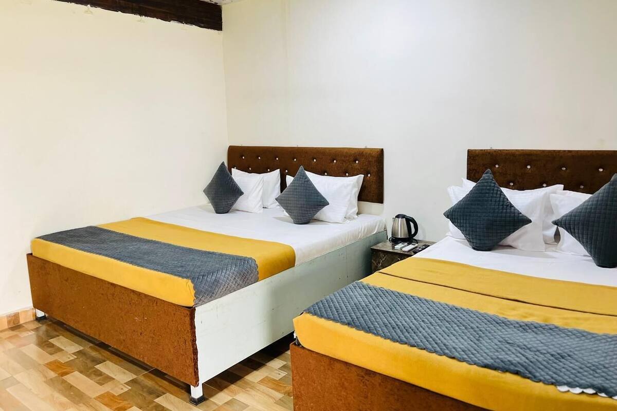 Een hotelkamer met twee bedden, elk voorzien van een houten hoofdbord, wit beddengoed en een geel-grijze deken.