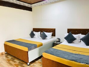 Une chambre d’hôtel avec deux lits, chacun doté d’une tête de lit en bois, de draps blancs et d’une couverture jaune et grise.