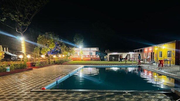 Une piscine dont le fond est recouvert de carrelage, entourée de bâtiments dont les fenêtres sont illuminées et dotés d’espaces de détente en plein air.