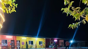 Un bâtiment bien éclairé, avec une façade aux couleurs vives, une pelouse devant et un arbre au premier plan.