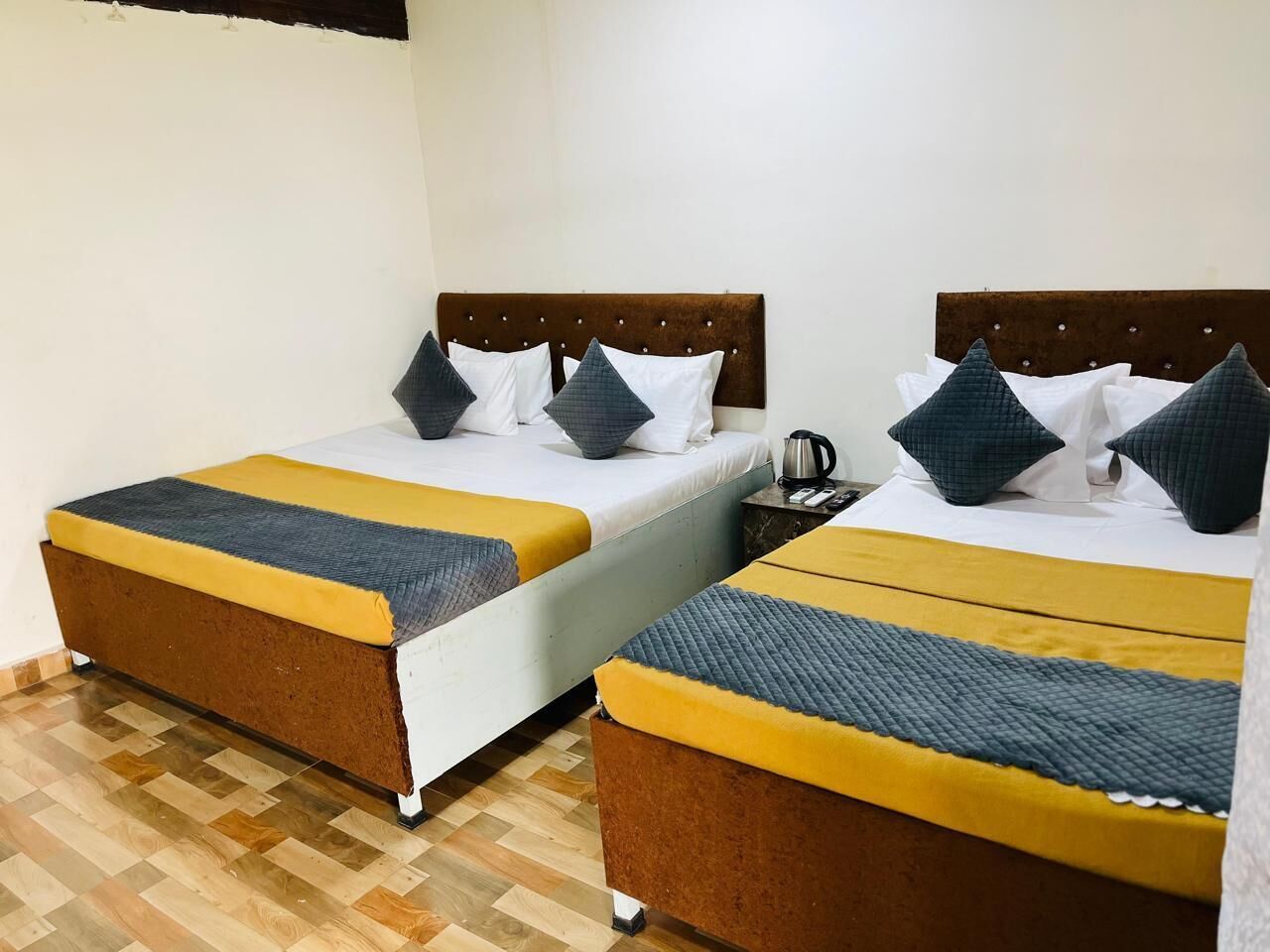Habitación de hotel con dos camas, cada una con cabecero marrón y colcha amarilla y gris.