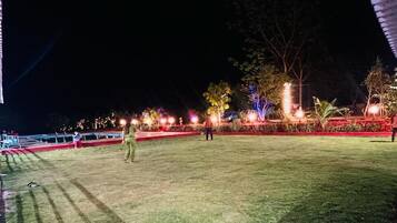 A nighttime outdoor area with a well-maintained lawn, decorative lighting, and a few people.