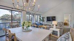 Amplia sala de estar con una gran mesa de comedor, asientos cómodos, un televisor y vista a un lago.