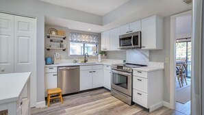 Una cocina moderna con armarios blancos, electrodomésticos de acero inoxidable y un taburete de madera.